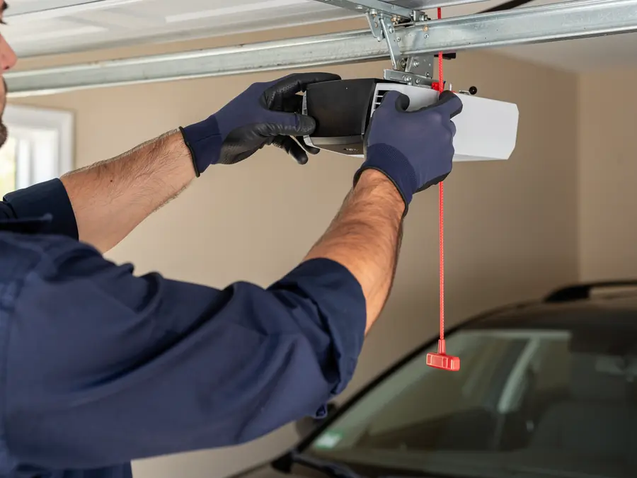 A technician in gloves is installing a garage door opener.